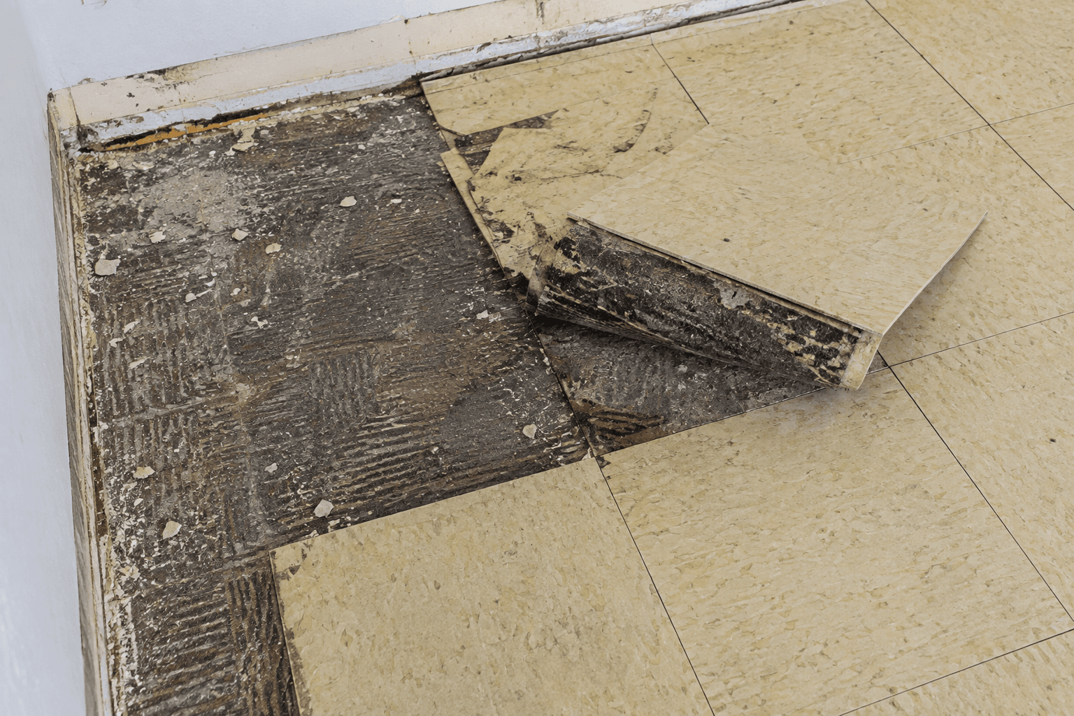 Plancher de tuiles anciennes partiellement retiré, révélant un adhésif noir et une surface de sous-plancher pendant des travaux de rénovation