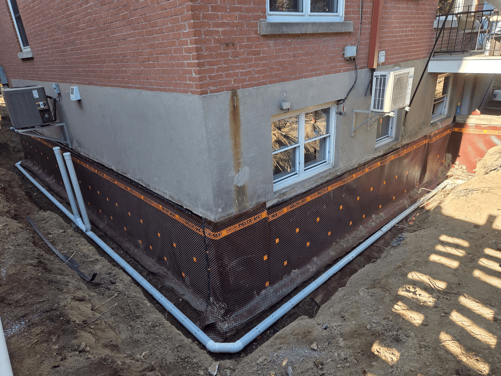  Installation d’un drain français autour des fondations d’une maison en brique avec membrane drainante, tuyaux perforés et excavation périphérique