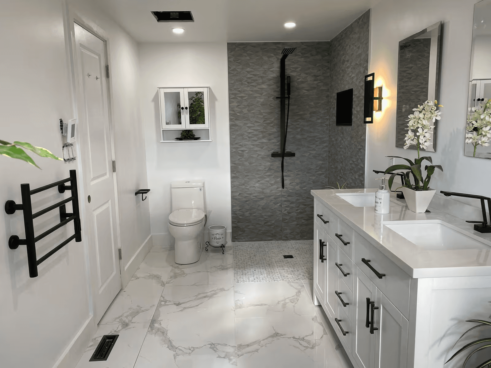 Salle de bain moderne rénovée avec meuble-lavabo double, douche à l’italienne carrelée, robinetterie noire, toilette et plancher effet marbre