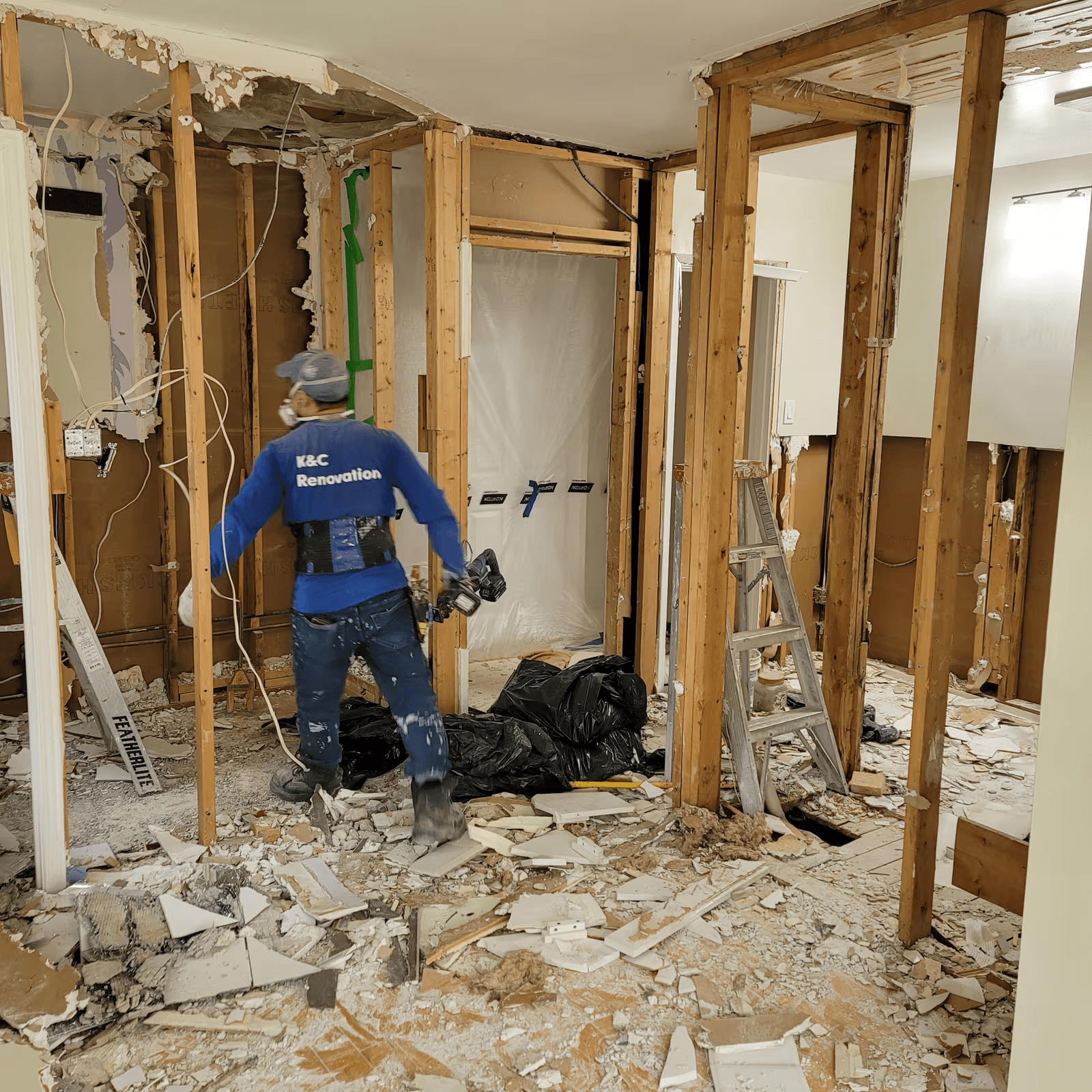 Travaux de démolition intérieure avec murs ouverts, colombages apparents et entrepreneur en rénovation retirant des débris.