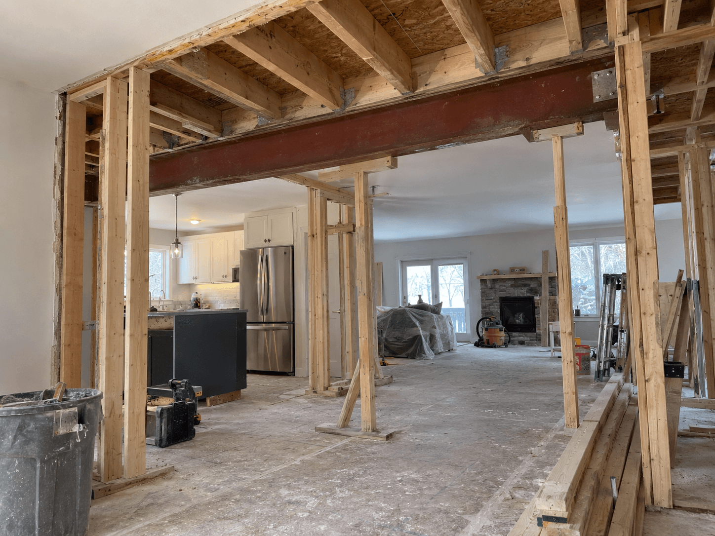 Maison en rénovation intérieure avec grande ouverture structurale renforcée par une poutre d’acier, charpente de bois apparente et poteaux temporaires de soutien