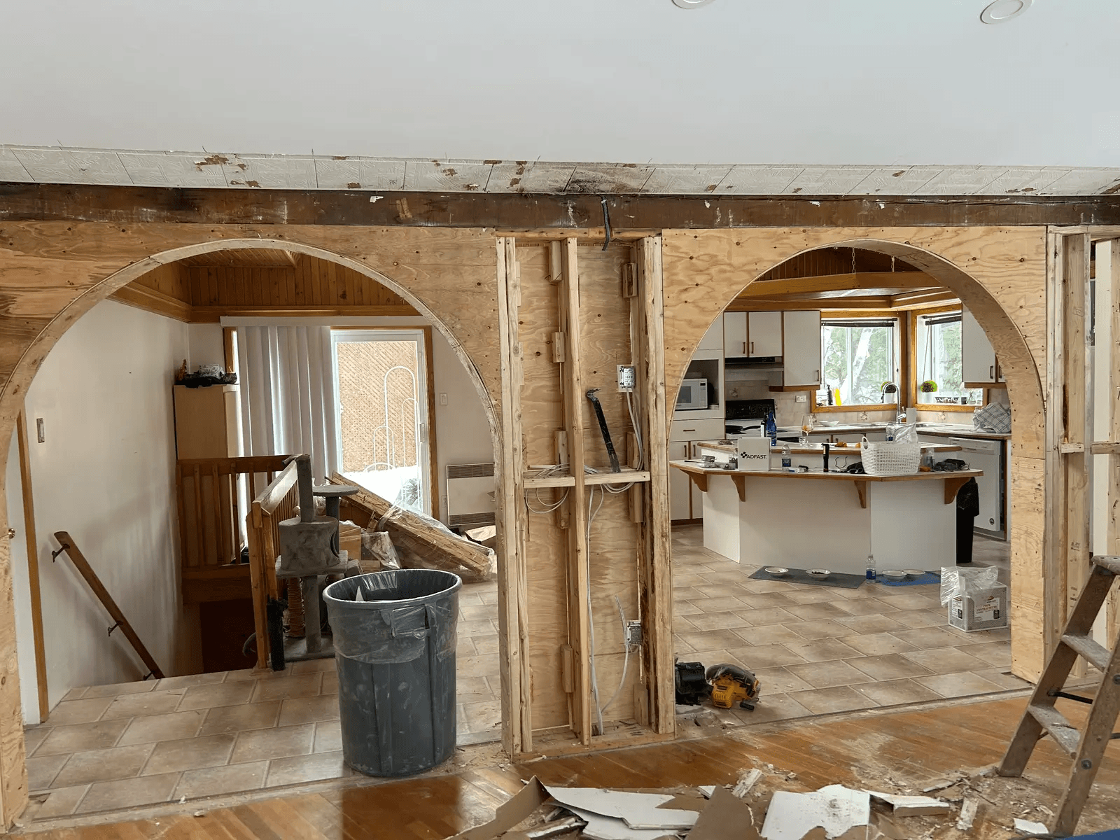 Rénovation intérieure d’une maison avec murs ouverts, grandes arches structurales en bois, charpente apparente, câblage visible et zone de cuisine en transformation