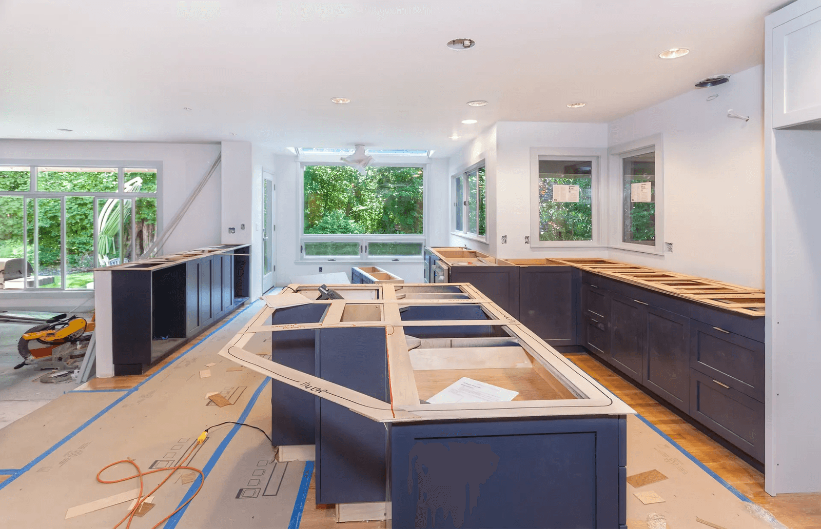  Cuisine résidentielle en rénovation avec armoires bleu foncé, grand îlot central en cours d’installation, surfaces protégées et éclairage encastré